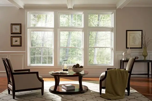 Triple white Alside double-hung windows with grids in a sunlit, wood-view living room.