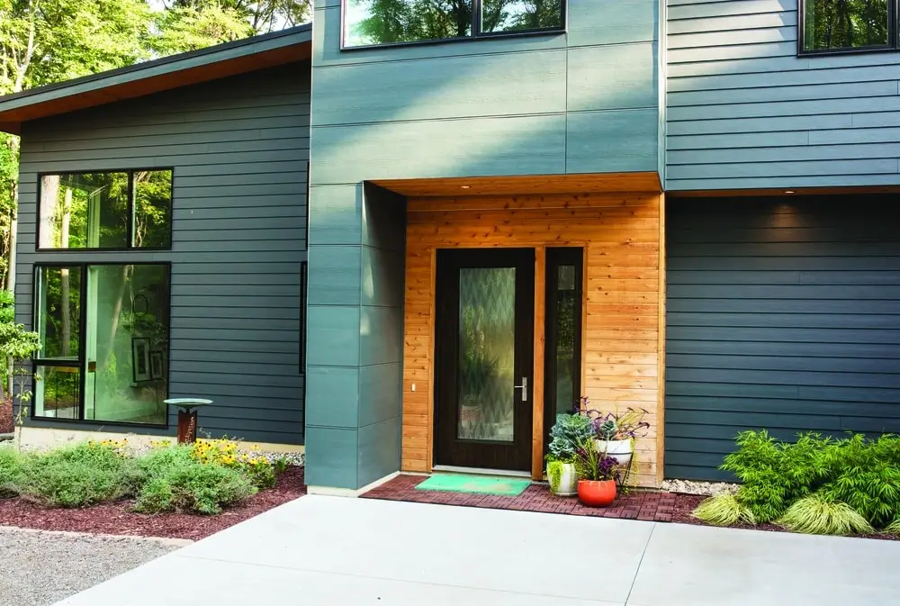 Contemporary house with a modern front door, gray siding, and wooden accents, blending natural materials with sleek design.