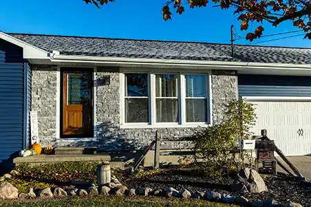 A charming blue house with Siding, a garage, and a sturdy stone wall.