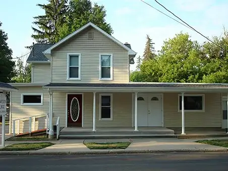 House with beige vinyl Siding, white trim, and covered front porch