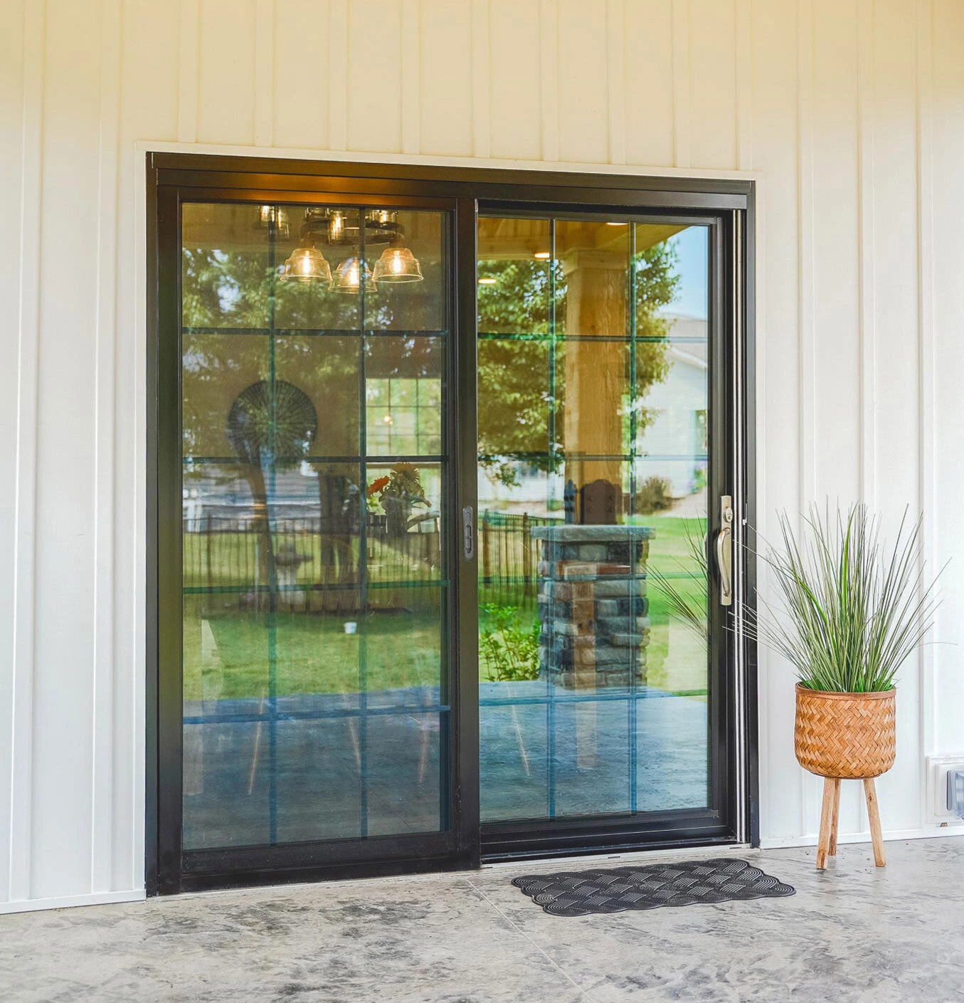 A dark bronze-framed sliding glass patio door with a full rectangular grid pattern, installed in a white vertical board-and-batten exterior wall.