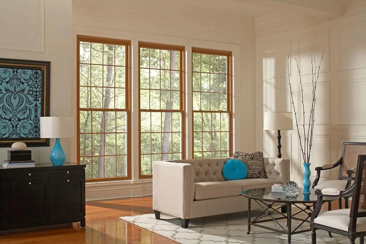 Three large wood-framed double-hung windows in a cream living room with a beige sofa and blue accents.