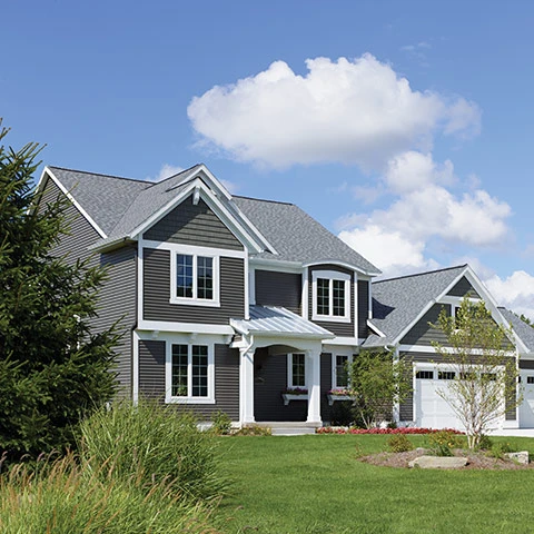 A two-story suburban house with dark grey horizontal vinyl siding, white trim, and a grey shingled roof under a blue sky.